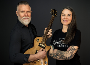 Man holding a guitar next to a woman with tattoos on a dark background