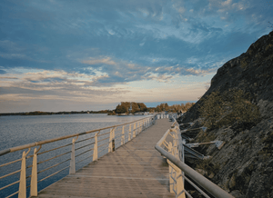 Wooden boardwalk extending over water with a rocky cliff and trees in the background